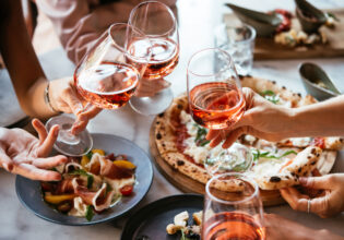 Friends enjoy a dinner party with pizza and rose wine in a bar or a restaurant.