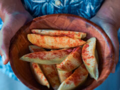 a hand holding a bowl filled with sliced mangoes sprinkled with salty plum powder