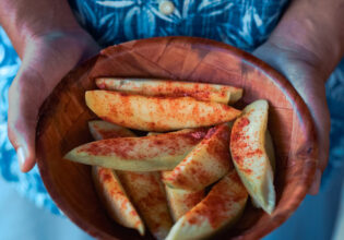 a hand holding a bowl filled with sliced mangoes sprinkled with salty plum powder