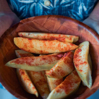 a hand holding a bowl filled with sliced mangoes sprinkled with salty plum powder