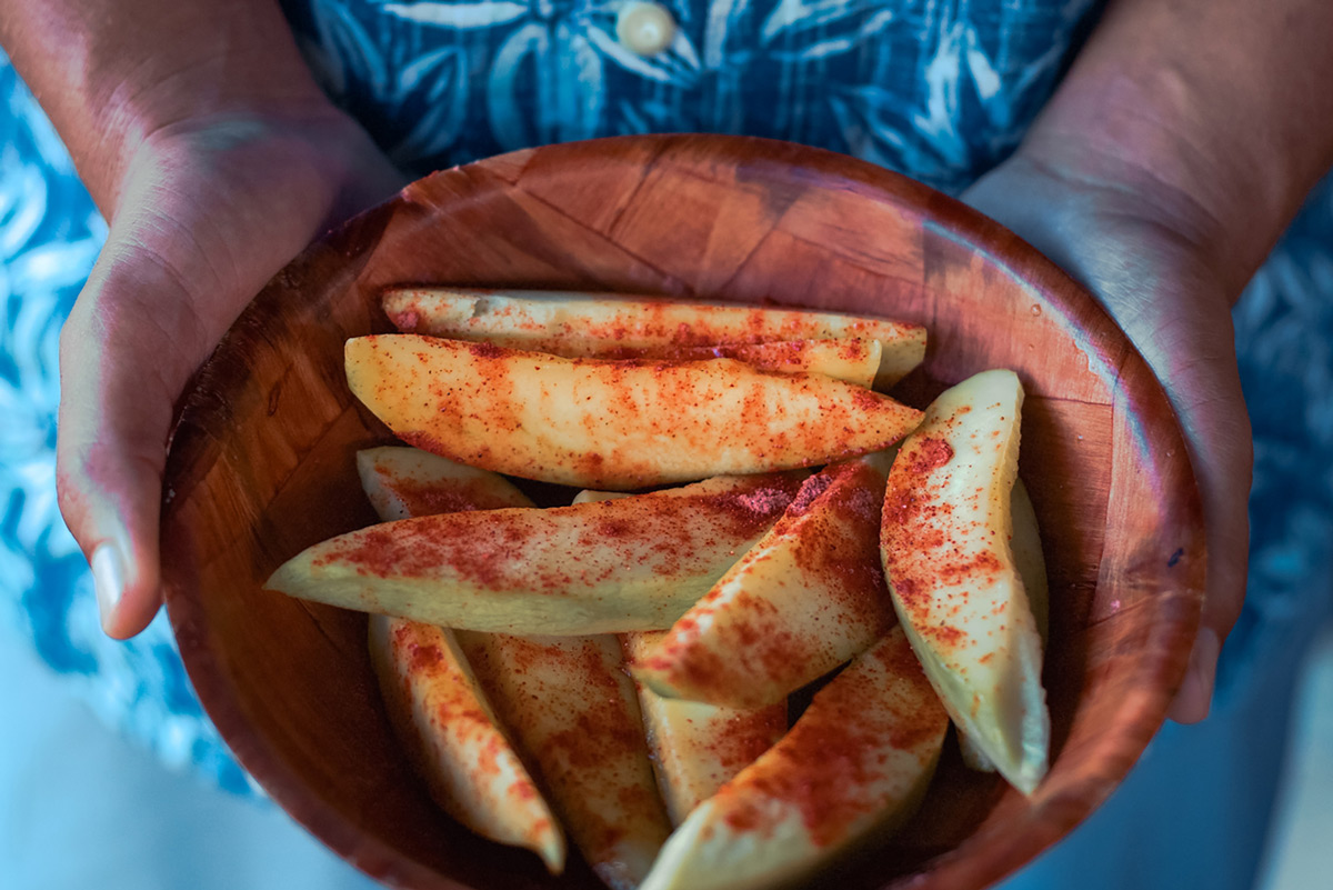 a hand holding a bowl filled with sliced mangoes sprinkled with salty plum powder