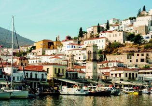 Wide shot of boats on Hydra Harbour with buildings around. Greece.