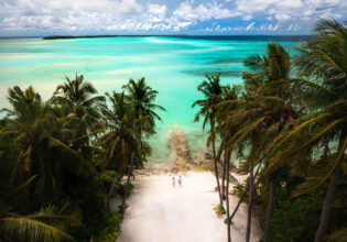 a couple walking hand in hand on the pristine white sand beach surrounded by palm trees in the Maldives